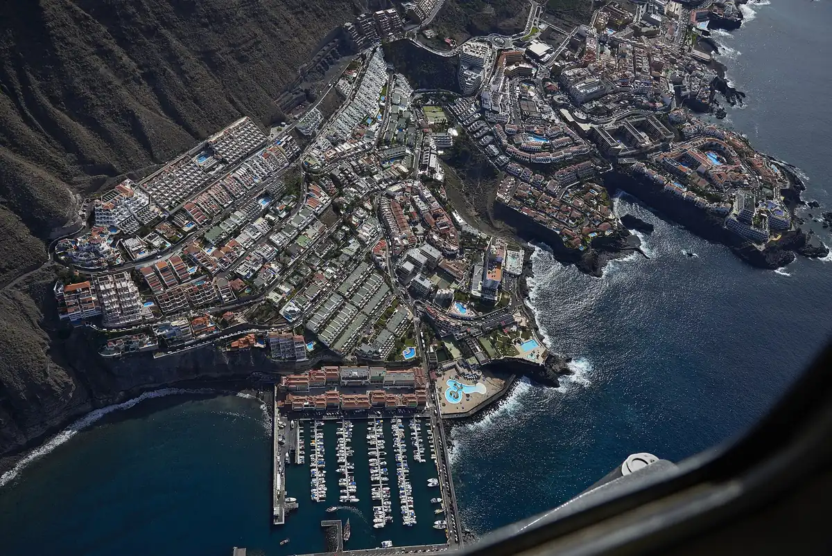 Vista aérea del puerto deportivo de Los Gigantes con la playa de arena negra a su lado y el pueblo en la ladera