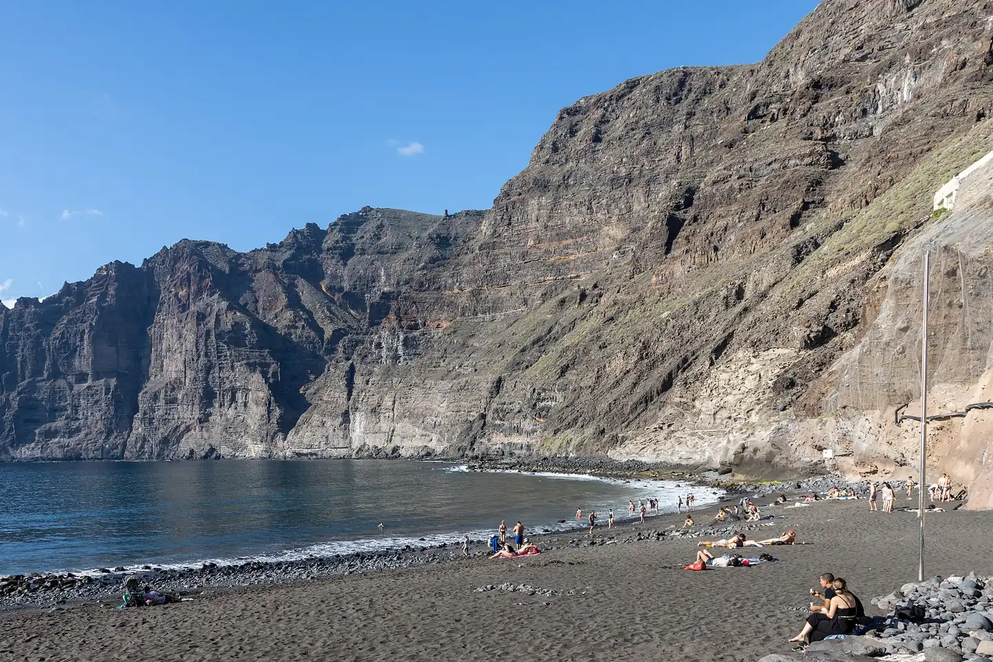Playa de Los Guíos de arena negra al pie de los acantilados de Los Gigantes, con bañistas en la orilla